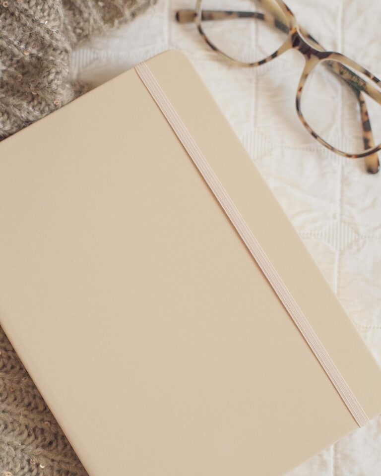 A warm and inviting composition featuring a notebook, glasses, and a sweater.
