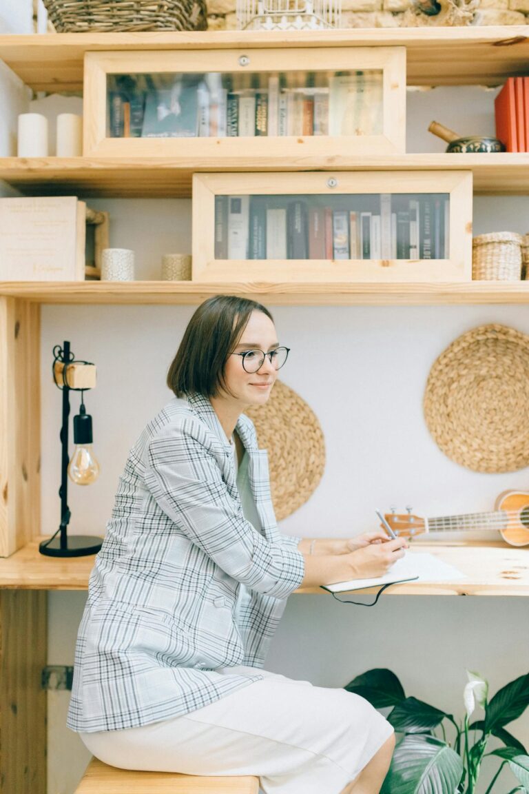 A young adult woman writing in a home office with bookshelves and decor.